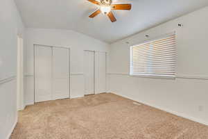 Unfurnished bedroom with two closets, ceiling fan, light colored carpet, and lofted ceiling