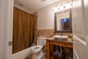 Basement bedroom bathroom featuring sink, shower / tub combo, tile walls, and toilet