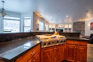 Kitchen with hanging light fixtures, dark stone countertops, a fireplace, and stainless steel gas cooktop