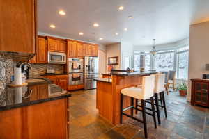 Kitchen featuring sink, stainless steel appliances, a kitchen breakfast bar, backsplash, and decorative light fixtures