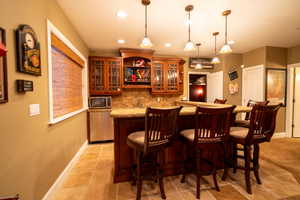 Bar featuring pendant lighting, backsplash, light colored carpet, sink, and light stone counters