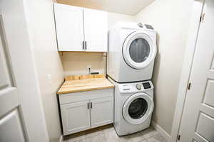 Laundry room featuring cabinets, light tile patterned floors, and stacked washer and dryer