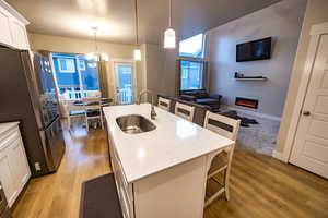 Kitchen with sink, stainless steel fridge, an island with sink, pendant lighting, and white cabinets