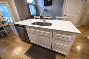 Kitchen featuring sink, light hardwood / wood-style flooring, stainless steel dishwasher, a kitchen island with sink, and white cabinets