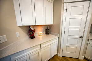 Bar with light stone countertops, hardwood / wood-style floors, and white cabinets