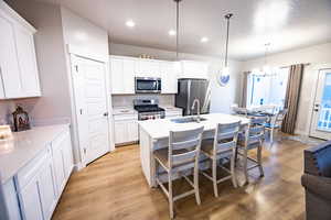 Kitchen featuring light hardwood / wood-style floors, white cabinetry, pendant lighting, and appliances with stainless steel finishes