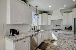 Kitchen featuring white cabinetry, sink, custom range hood, and stainless steel appliances