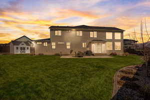 Back house at dusk featuring a lawn, a storage unit, and a patio area