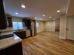 Kitchen with light stone countertops, light wood-type flooring, stainless steel appliances, and a wealth of natural light