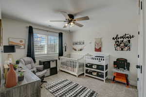 Carpeted bedroom featuring a nursery area and ceiling fan