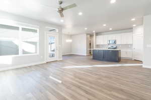 Unfurnished living room with ceiling fan with notable chandelier and light hardwood / wood-style floors