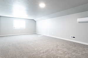 Interior space featuring a textured ceiling, carpet floors, a wall mounted AC, and lofted ceiling