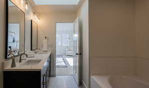 Bathroom featuring tile patterned floors, a skylight, vanity, and a relaxing tiled tub