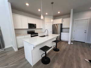 Kitchen featuring sink, white cabinetry, light stone counters, a center island with sink, and appliances with stainless steel finishes