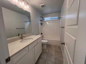 Full bathroom with vanity, tub / shower combination, a textured ceiling, and toilet