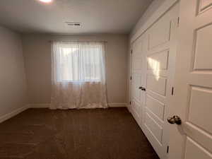 Unfurnished bedroom with dark colored carpet and a textured ceiling