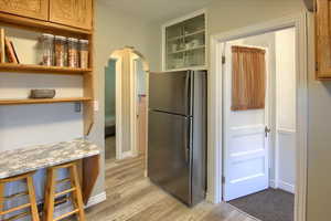 Kitchen with a breakfast bar area, stainless steel fridge, light hardwood / wood-style floors, and light stone counters