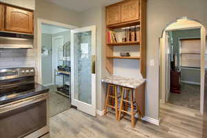 Kitchen with decorative backsplash, light hardwood / wood-style flooring, extractor fan, and stainless steel range with electric cooktop