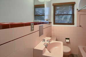 Bathroom with a bathing tub, sink, tile walls, and toilet