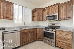 Kitchen with backsplash, light stone countertops, sink, and appliances with stainless steel finishes