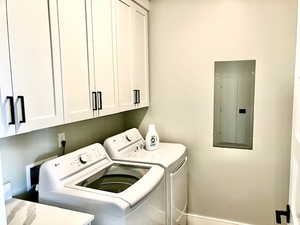 Clothes washing area with electric panel, cabinets, and washing machine and dryer