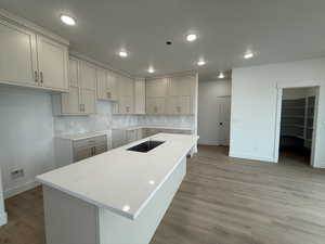 Kitchen featuring light stone countertops, backsplash, sink, light hardwood / wood-style floors, and a kitchen island