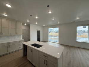 Kitchen featuring a center island, sink, light hardwood / wood-style flooring, decorative backsplash, and light stone countertops