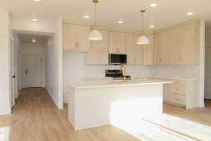 Kitchen featuring hanging light fixtures, decorative backsplash, stainless steel appliances, and a kitchen island with sink