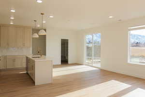 Kitchen with sink, light hardwood / wood-style flooring, backsplash, pendant lighting, and a center island with sink