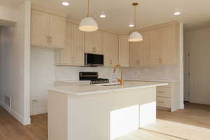 Kitchen featuring sink, stainless steel appliances, tasteful backsplash, light hardwood / wood-style floors, and a center island with sink