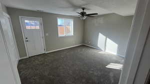 Entryway with a textured ceiling, dark carpet, and ceiling fan