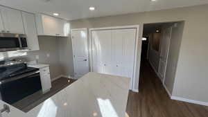 Kitchen with light stone countertops, appliances with stainless steel finishes, dark hardwood / wood-style floors, and white cabinetry