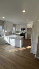 Kitchen featuring kitchen peninsula, appliances with stainless steel finishes, dark hardwood / wood-style flooring, sink, and white cabinetry