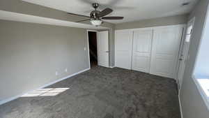 Unfurnished bedroom featuring dark colored carpet, ceiling fan, and multiple windows