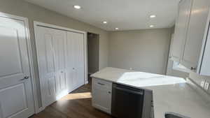 Kitchen featuring white cabinets, dark hardwood / wood-style flooring, stainless steel dishwasher, and light stone counters