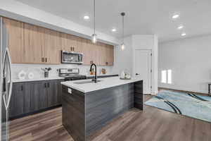 Kitchen featuring a kitchen island with sink, appliances with stainless steel finishes, decorative light fixtures, and dark hardwood / wood-style flooring