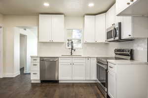 Kitchen featuring white cabinets, sink, decorative backsplash, dark hardwood / wood-style flooring, and stainless steel appliances