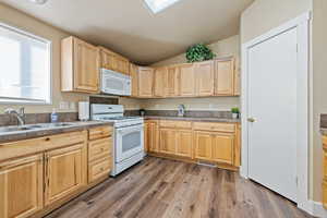 Kitchen featuring sink, light brown cabinets, wood-type flooring, vaulted ceiling, and white appliances