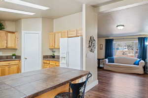 Kitchen featuring a textured ceiling, white fridge with ice dispenser, dark wood-type flooring, and light brown cabinetry