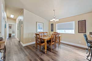 Dining room with a textured ceiling, hardwood / wood-style flooring, lofted ceiling with skylight, and a notable chandelier