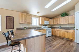 Kitchen featuring sink, kitchen peninsula, hardwood / wood-style floors, vaulted ceiling, and white appliances