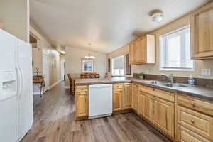 Kitchen featuring sink, kitchen peninsula, wood-type flooring, decorative light fixtures, and white appliances