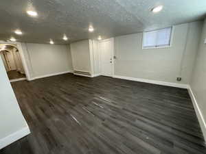 Basement with a baseboard heating unit, a textured ceiling, and dark wood-type flooring