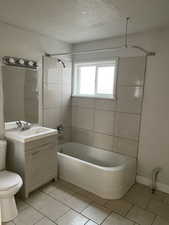 Full bathroom with a textured ceiling, vanity, tile patterned flooring, toilet, and tiled shower / bath