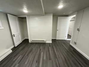 Basement with dark hardwood / wood-style flooring, a baseboard radiator, and a textured ceiling