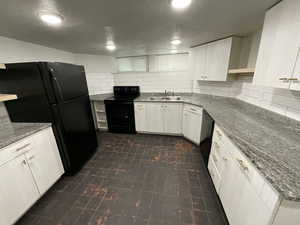 Kitchen with backsplash, dark stone counters, sink, black appliances, and white cabinets