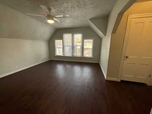 Bonus room with ceiling fan, vaulted ceiling, a textured ceiling, and dark wood-type flooring