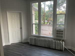 Unfurnished room featuring cooling unit, dark wood-type flooring, and radiator