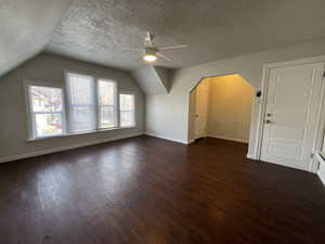 Additional living space featuring a textured ceiling, ceiling fan, dark wood-type flooring, and vaulted ceiling