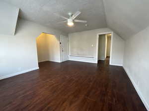 Additional living space with dark wood-type flooring, a baseboard heating unit, vaulted ceiling, ceiling fan, and a textured ceiling